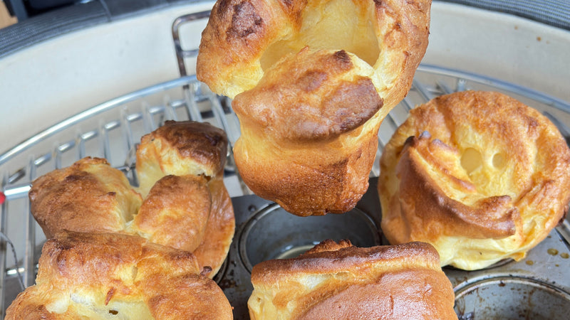 Golden jumbo Yorkshire puddings in a baking tin on a kamado cooking grate.