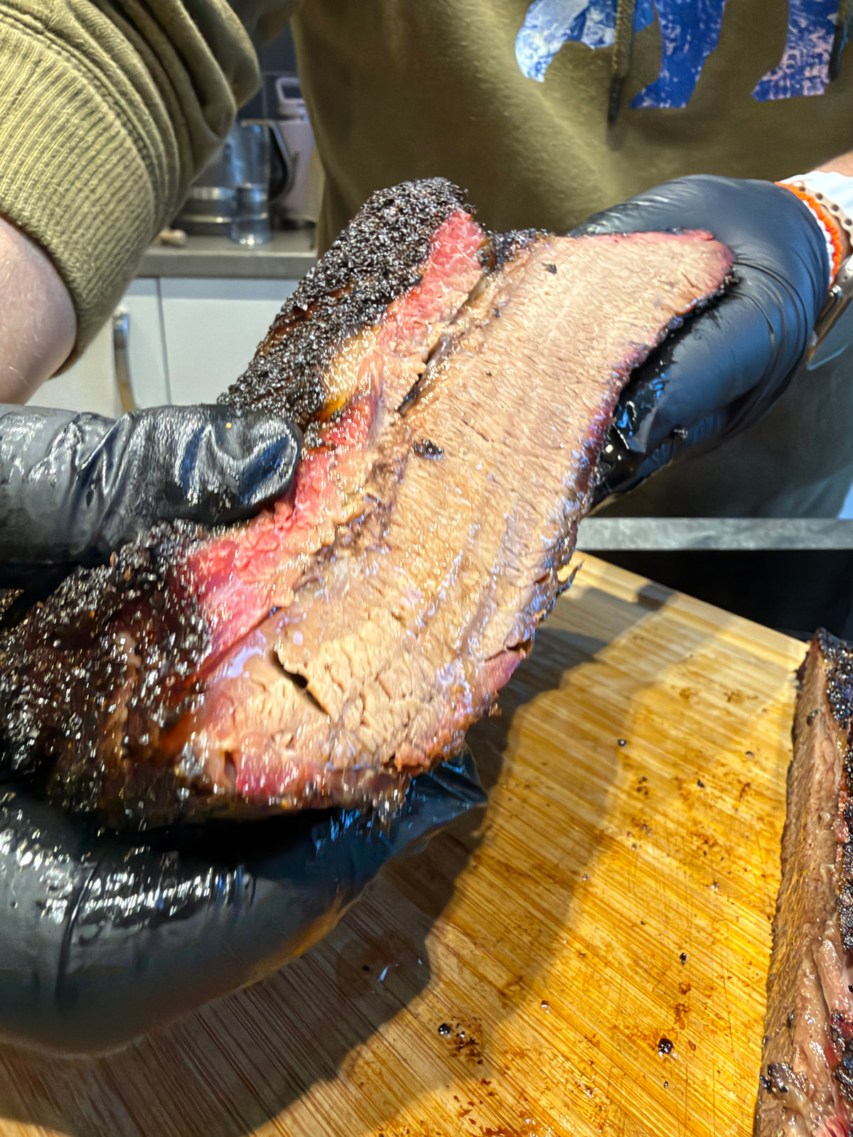 Gloved hands holding sliced smoked brisket to show its bark and pink smoke ring.