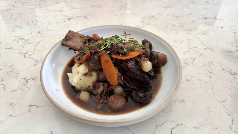 Short-rib bourguignon served with mashed potatoes, carrots and mushrooms in a shallow bowl.