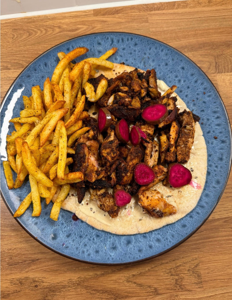 Chicken shawarma served on flatbread with fries and pink pickles on a blue plate.