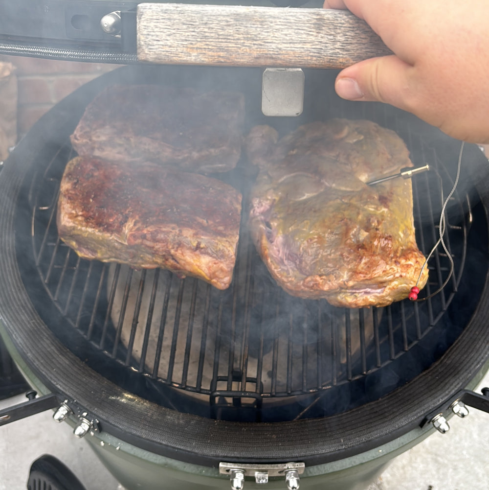 Two large cuts of meat cooking with temperature probes inside a smoking kamado.