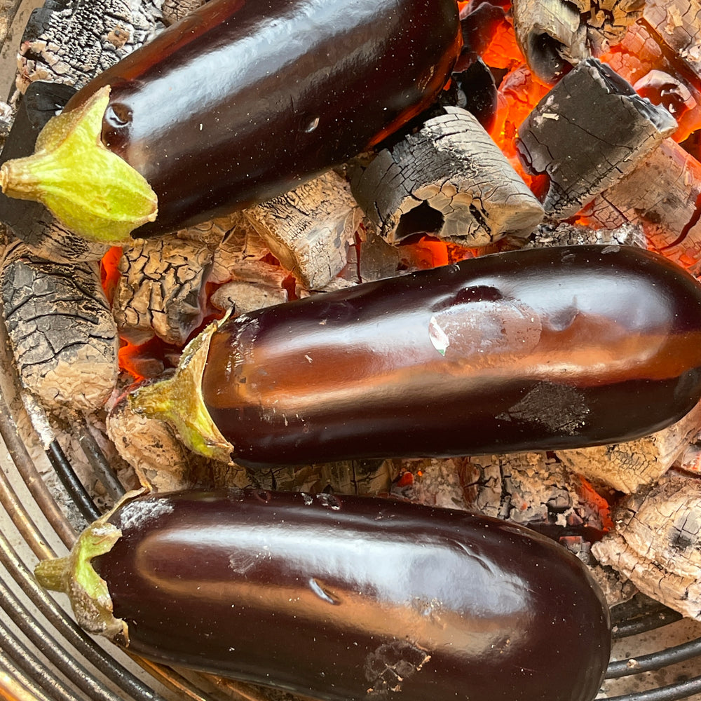 Whole aubergines cooking directly on glowing charcoal.