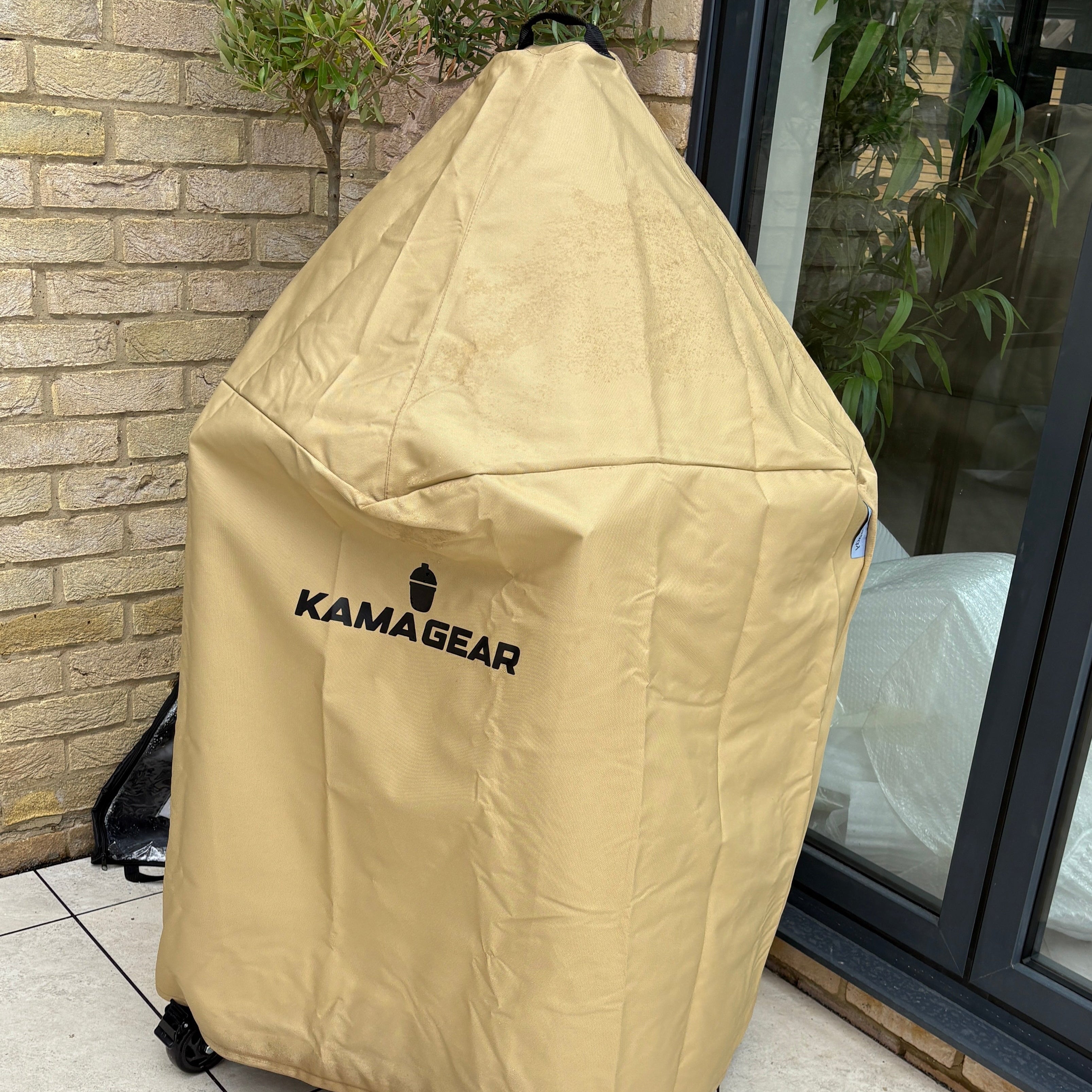 Beige Kama Gear cover on a grill against a brick wall.
