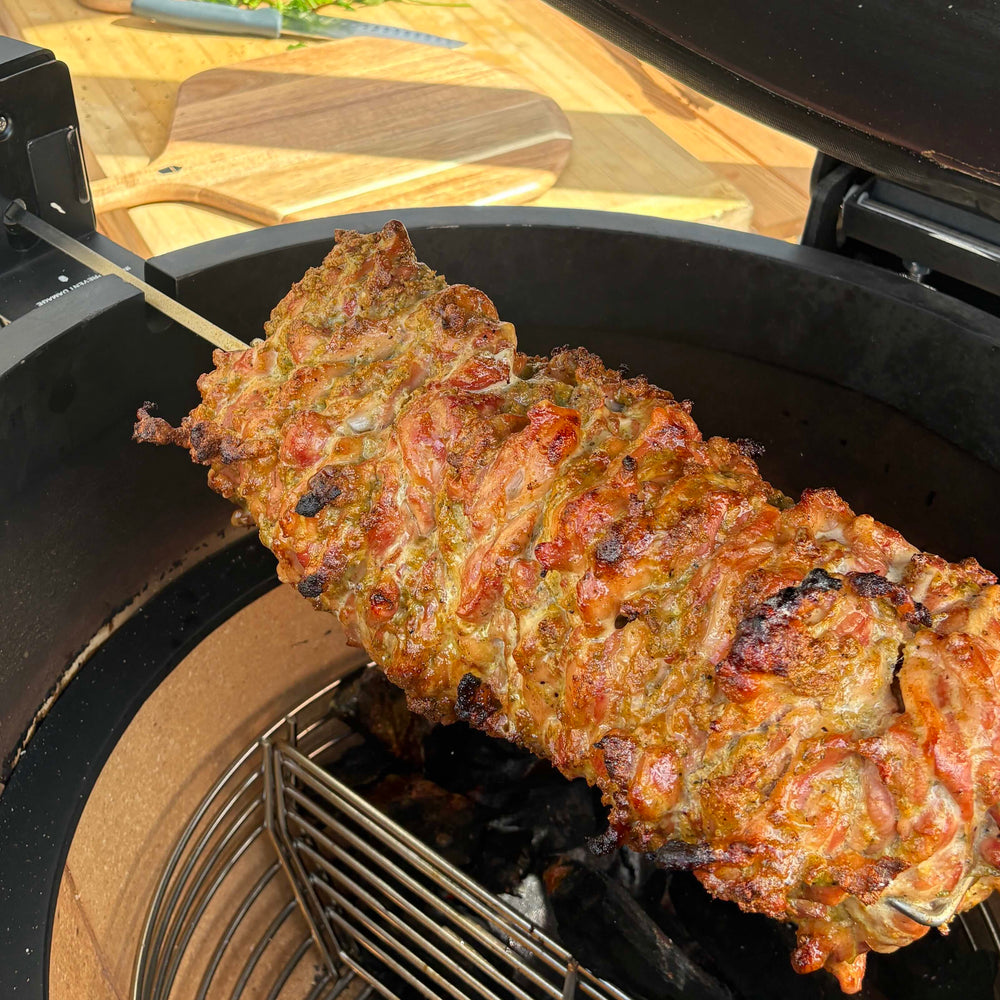 Chicken shawarma turning on a rotisserie spit inside an open kamado.