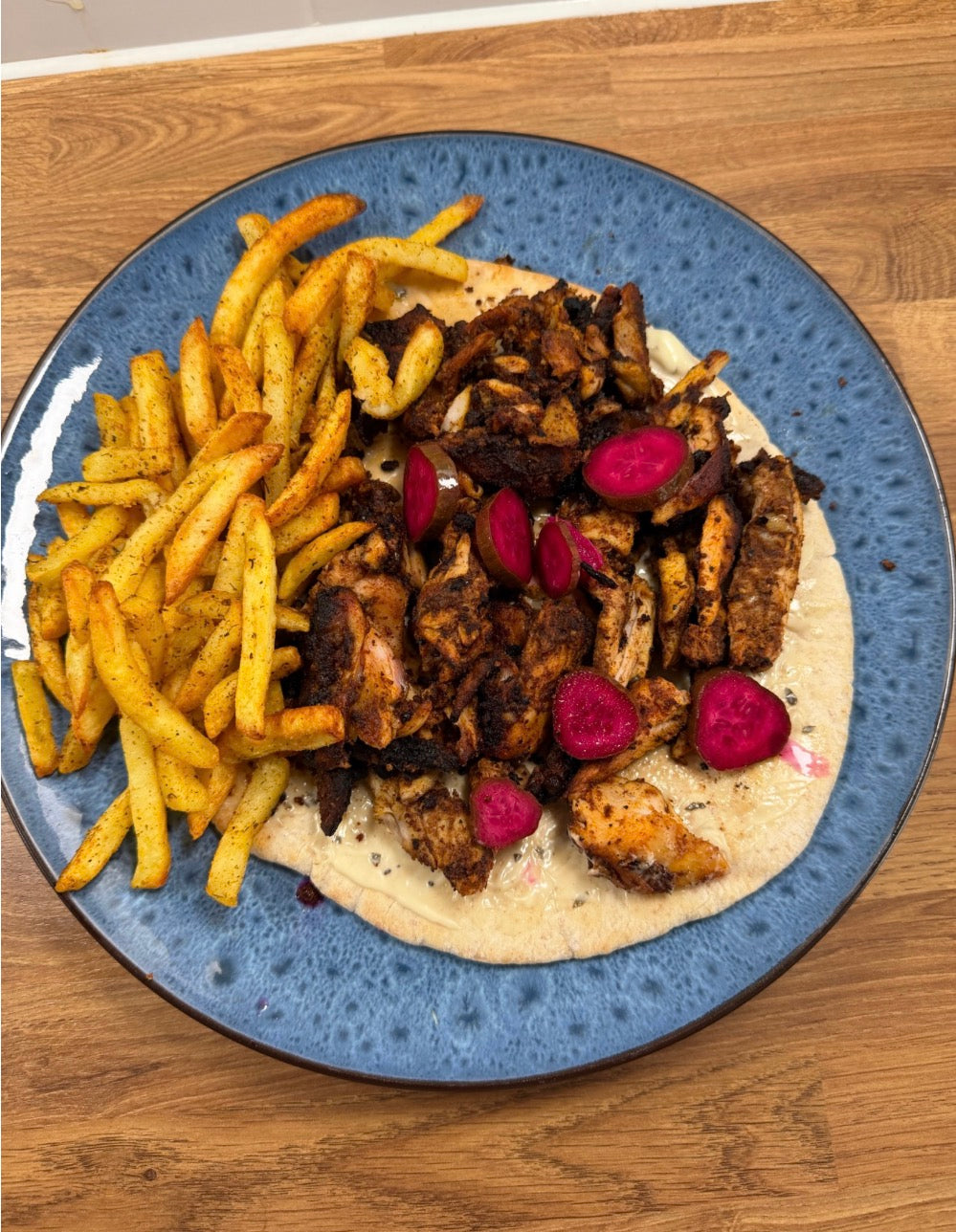 Chicken shawarma served on flatbread with fries and pink pickles on a blue plate.